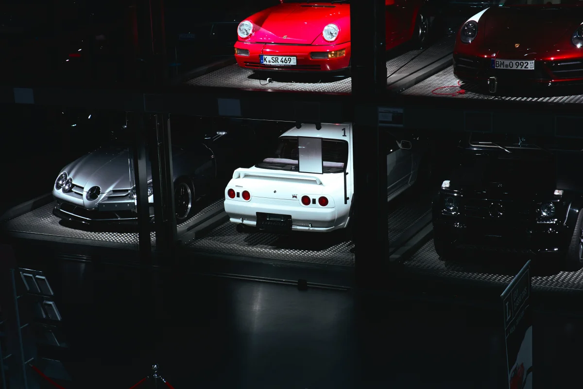 Premium car storage facility featuring exotic vehicles including Porsche 911, Nissan GT-R, and Mercedes-Benz on diamond-plate flooring with professional lighting